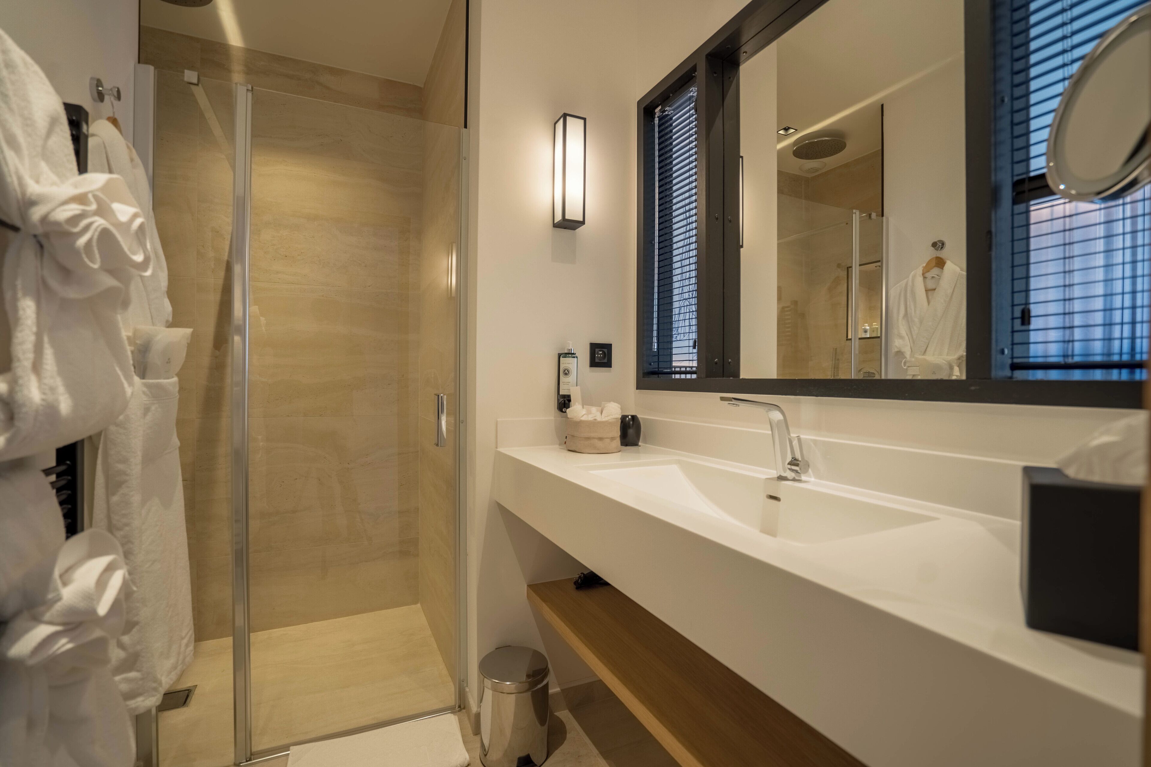 A modern bathroom with a glass-enclosed shower, a large mirror, and a white sink.