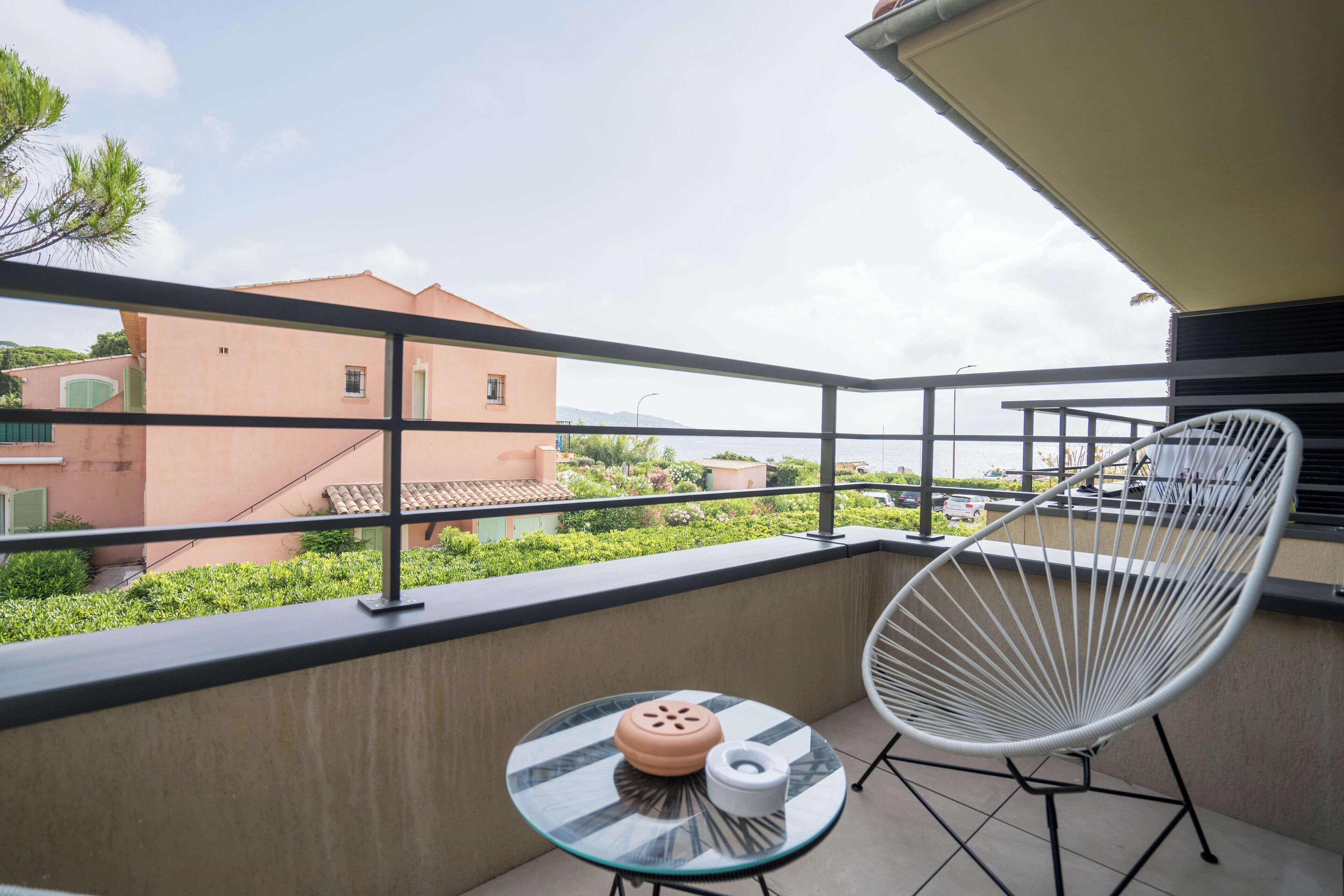 Un balcón con una mesa de vidrio, una silla blanca y vistas de edificios cercanos.