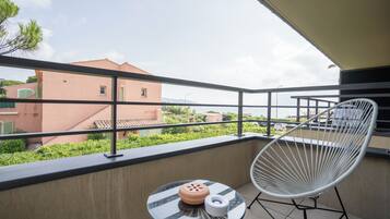 Un balcón con una mesa de vidrio, una silla blanca y vistas de edificios cercanos.