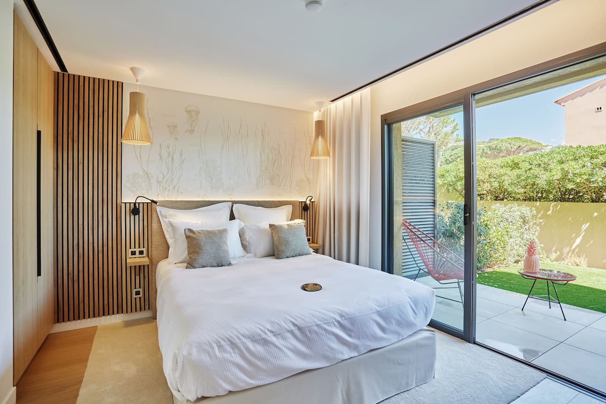 A modern bedroom with a large bed, a wooden slat wall, and a sliding glass door to a patio.
