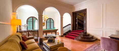 A spacious lobby with a yellow sofa, a pool table, and a staircase leading to an upper floor.