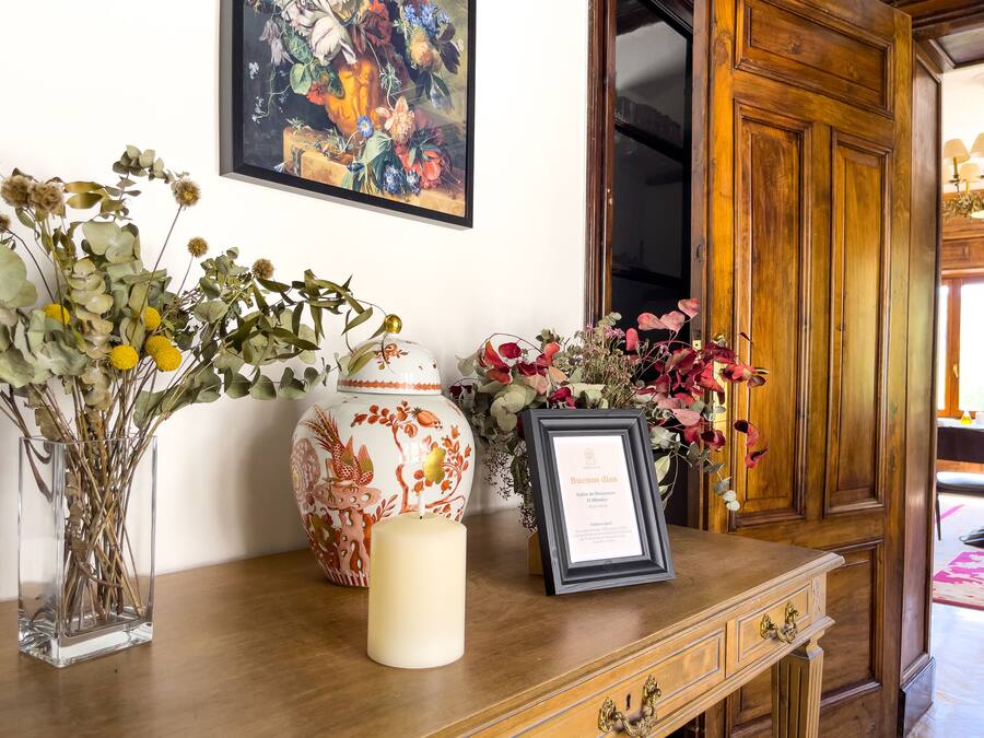 Un escritorio de madera con un certificado enmarcado, un jarrón decorativo y un jarrón con flores secas.