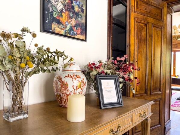 A wooden desk with a framed certificate, a decorative vase, and a clear vase with dried flowers. - Angelats Hotel (Ribes De Freser)