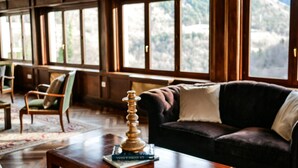 A cozy living room with a dark-colored sofa, a wooden coffee table with books, and a view of a mountainous landscape through large windows. - Angelats Hotel (Ribes De Freser)