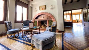 A spacious living room with a fireplace, comfortable seating, and a large window. - Angelats Hotel (Ribes De Freser)