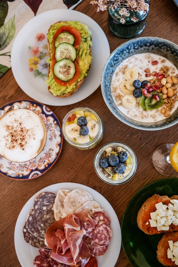 A variety of food items including sandwiches, a bowl of yogurt with fruits, and a plate of cured meats.