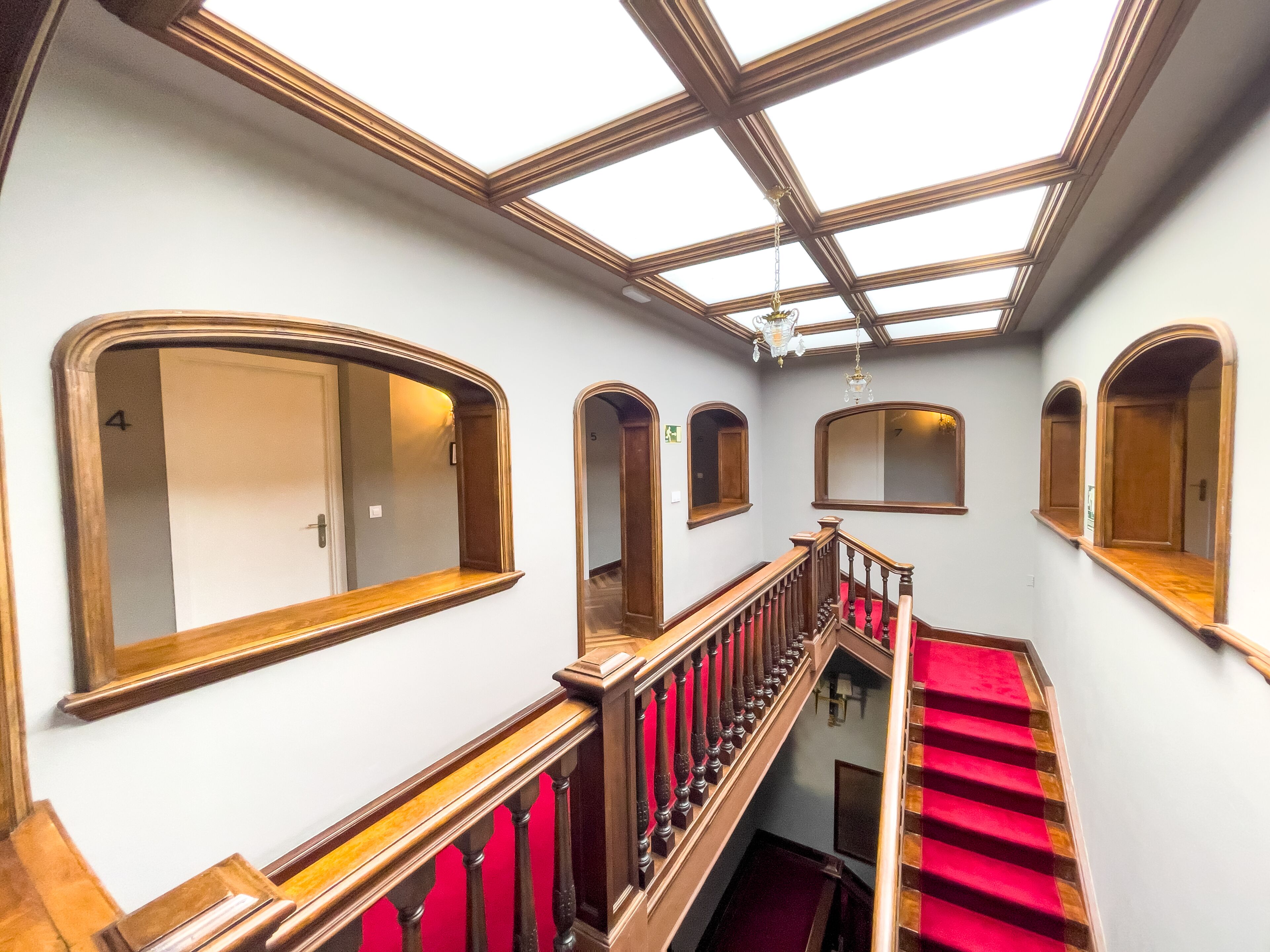 A grand staircase with a red carpet, wooden railings, and a skylight above.