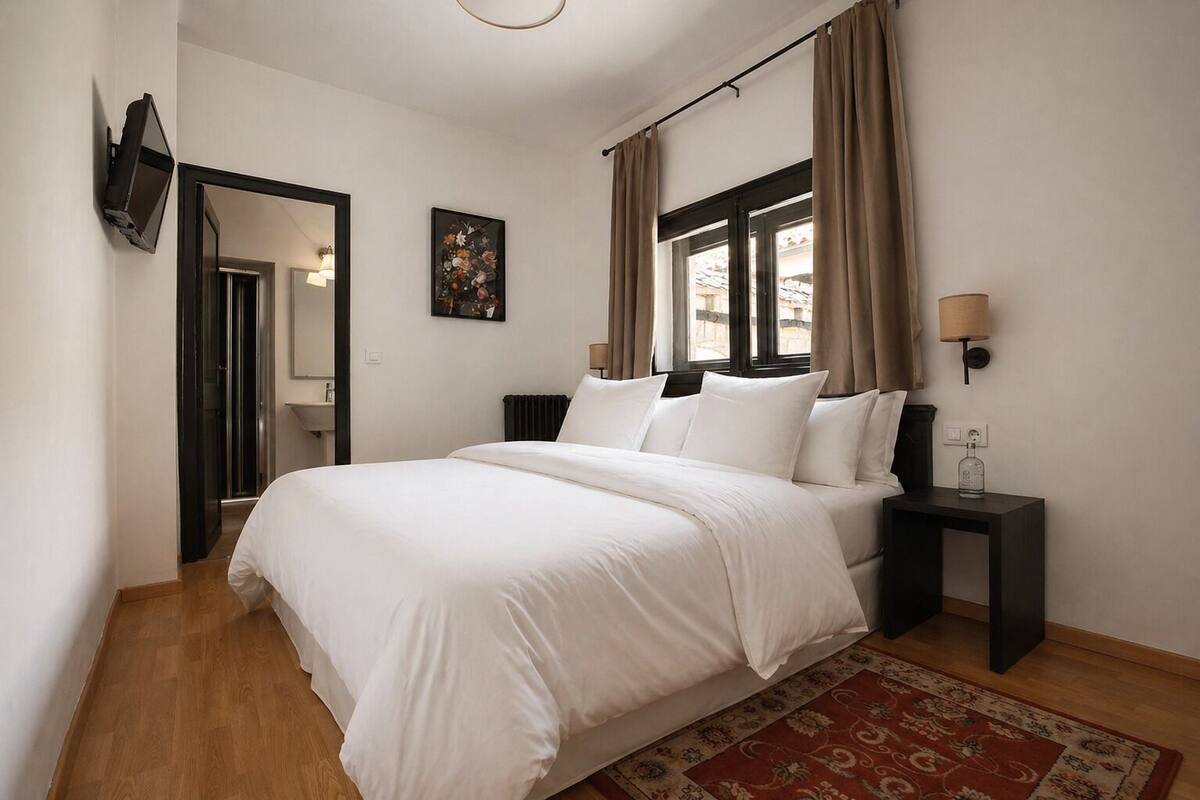 Een slaapkamer met een bed, een nachtkastje, een lamp, een spiegel en een raam met gordijnen.