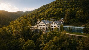 Un grand immeuble à étages, doté d’une façade symétrique, entouré d’une forêt dense et d’un lac.