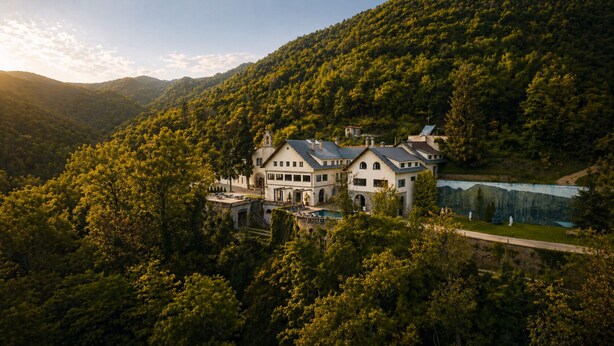 A large, multi-story building with a symmetrical facade, surrounded by dense forest and a lake. - Angelats Hotel (Ribes De Freser)