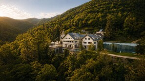 A large, multi-story building with a symmetrical facade, surrounded by dense forest and a lake. - Angelats Hotel (Ribes De Freser)