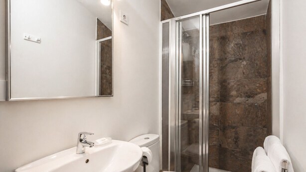 Une salle de bain moderne avec un lavabo, des toilettes et une douche à l’italienne, le tout de couleur blanche.