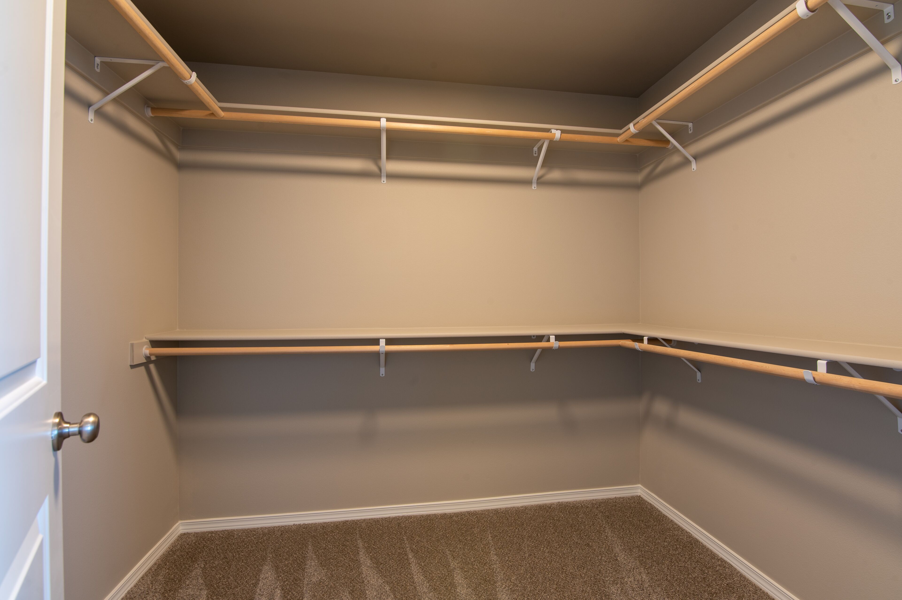 A closet with wooden rods and metal brackets, carpeted floor, and a door with a silver handle.