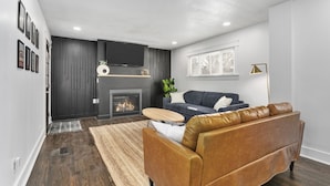 Een moderne woonkamer met een open haard, een bank, een salontafel en een aan de muur bevestigde televisie.