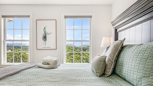 A neatly made bed with a quilted green bedspread, two windows with a view of greenery, and a framed artwork on the wall. - Castlewood Retreat | Views, Hot Tub & Foosball Table🛁🏔️ + Biltmore Pass (Alexander)