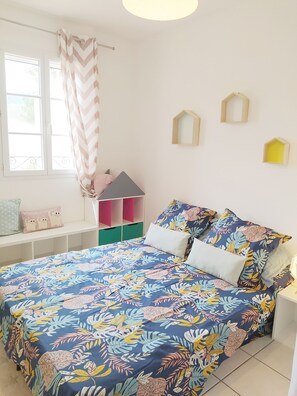Um quarto com uma cama, uma janela com cortinas, uma pequena decoração de madeira e uma prateleira na parede.
