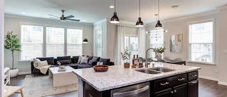 A modern kitchen with a large island, dark cabinetry, and pendant lighting.