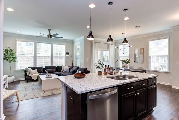 A modern kitchen with a large island, dark cabinetry, and pendant lighting.
