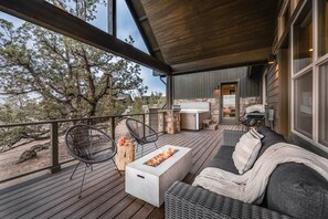 A wooden deck with a fire pit, outdoor seating, and a stone fireplace. - Hot Tub & Golf Access Nearby | Starview at Brasada Ranch Resort by AvantStay (Powell Butte)