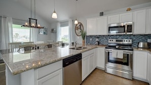 A modern kitchen with white cabinets, granite countertops, stainless steel appliances, and pendant lighting. - Crustacean Station- Private Pool - Cart Discount (Port Aransas)