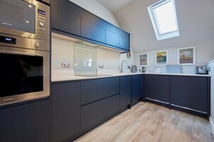 A modern kitchen with dark cabinetry, a built-in oven, a large window, and artwork on the walls.