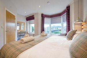 A bedroom with a large bed, a desk, and a window with curtains.