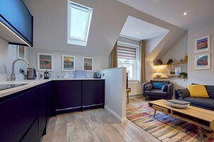 A modern kitchen with a central island, a dining area with a sofa and coffee table, and a living room with a fireplace.