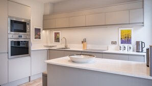 A modern kitchen with built-in appliances, a large island, and artwork on the walls. - Howe Keld 5 First Floor (Keswick)
