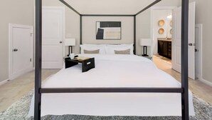 A four-poster bed with white linens, a bedside table with a book and a cup, and a modern abstract painting on the wall.