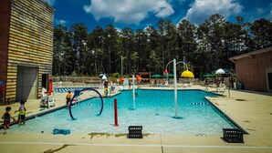 A swimming pool with a water slide, surrounded by trees and a building with a sloped roof.
