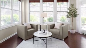A corner living room with two beige sofas, a round coffee table, a floor lamp, and a potted plant.