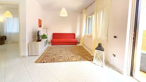 Un salon moderne avec un canapé rouge, un tapis à motifs, une petite table d’appoint et un téléviseur.