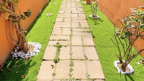 Un étroit sentier bordé de murs orange et d’herbe verte, qui mène à un bâtiment doté d’un toit recouvert de tuiles.