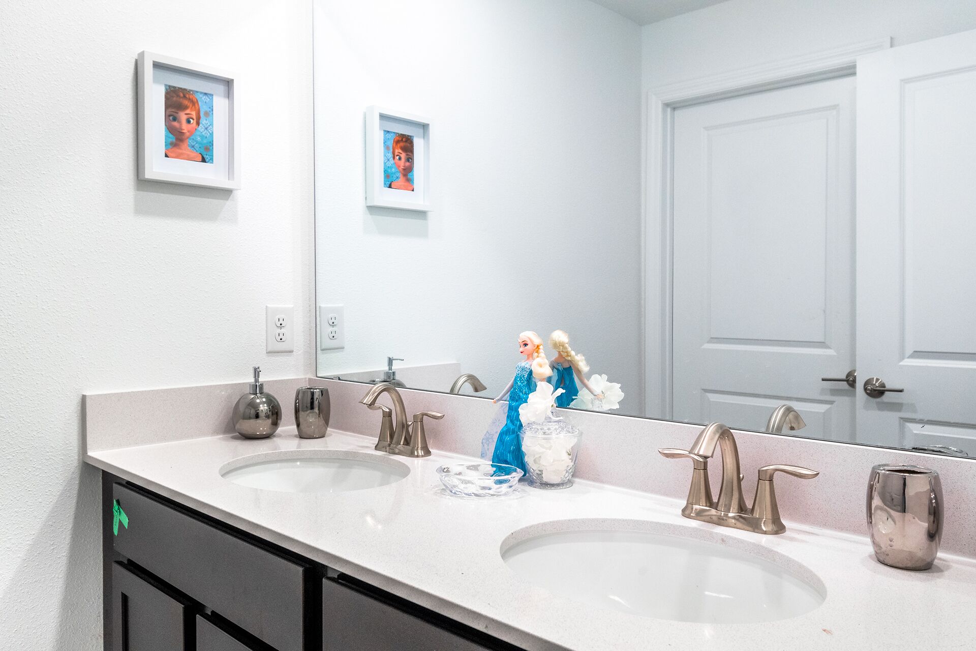 A bathroom with two sinks, a large mirror, and framed pictures on the wall.
