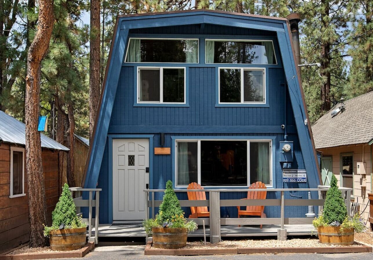 Eine zweistöckige, blaue Holzhütte mit Veranda, zwei Fenstern und einer Tür.