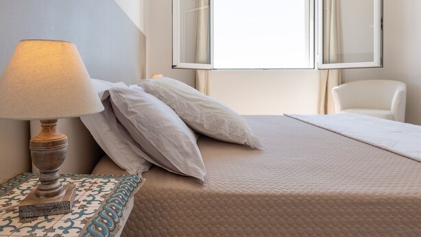 A hotel room with a bed, a chair, a lamp, and a window with curtains. - Panoramic Studio Carloforte (Carloforte)