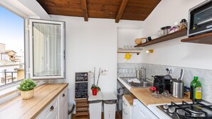 A compact kitchen with a wooden ceiling, a window with curtains, a sink, a stove, and a small refrigerator.