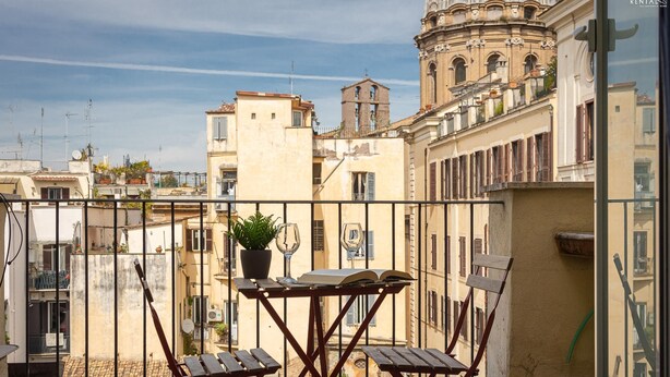 A balcony with a table and chairs, a potted plant, and a view of historic buildings.