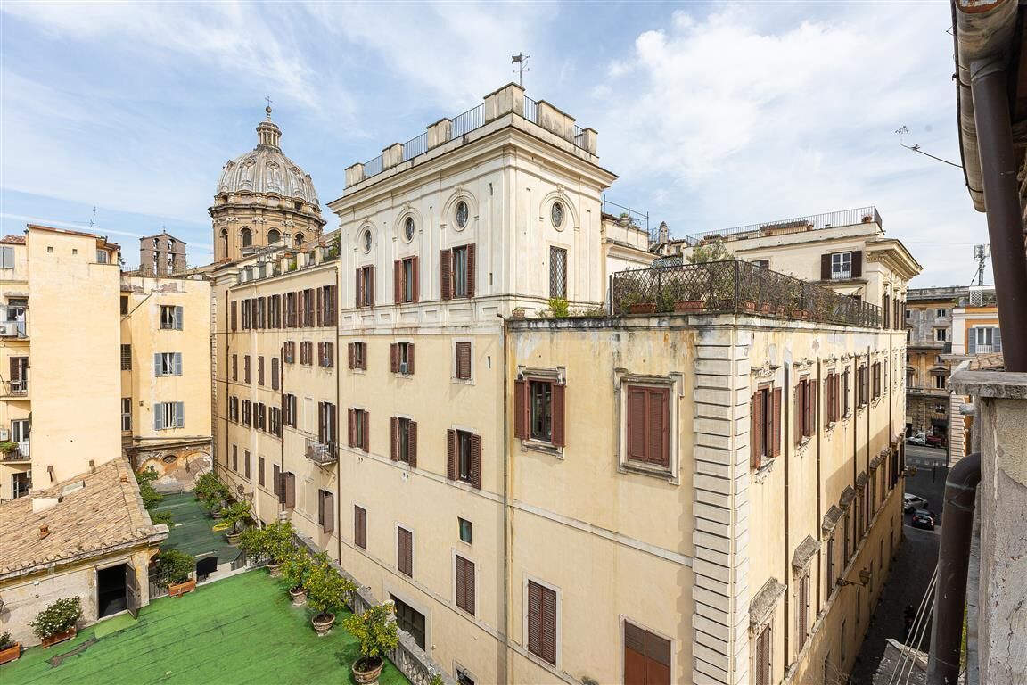 A historic building with a central dome, multiple windows, and a courtyard with greenery.