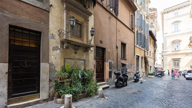 Una calle empedrada con edificios históricos, una moto estacionada afuera y algunos peatones.