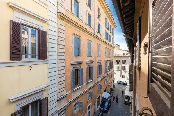 A narrow street with buildings featuring traditional architecture, including shuttered windows and balconies.