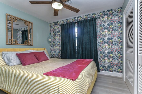 Une chambre à coucher avec un lit, un ventilateur de plafond, un grand miroir et des rideaux à motifs.