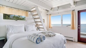 Un dormitorio con cama, ventana con cortinas y vista al mar, además de una escalera de madera.