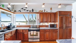 Enjoy a scenic view of the water from this kitchen's large window, featuring a stainless steel stove and microwave.