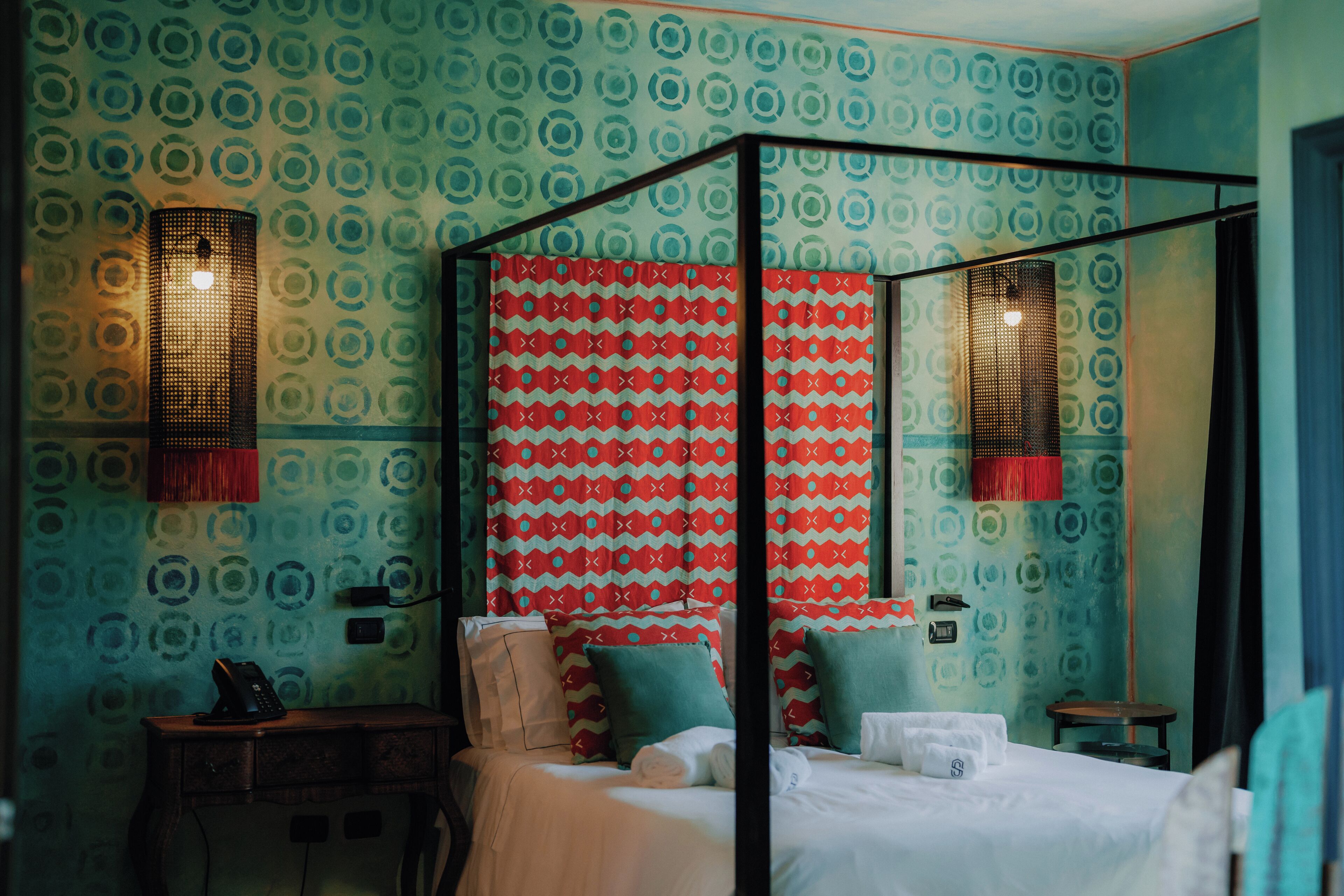 Una cama con dosel, un espejo, un teléfono en un escritorio y papel tapiz estampado.