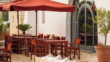 Un espace extérieur aménagé avec des tables et des chaises en bois, des parasols rouges et des plantes en pot.