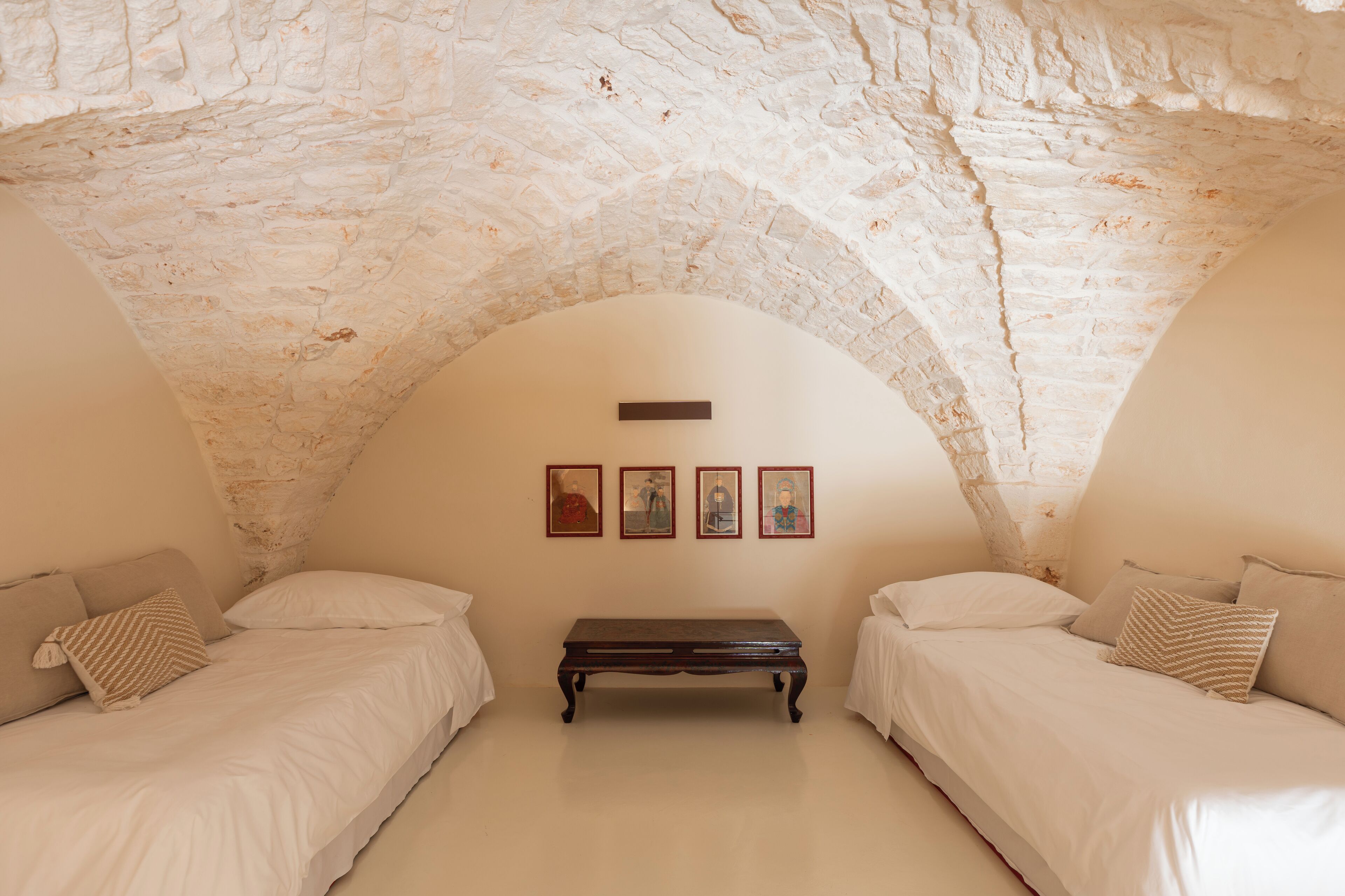 Een kamer met twee bedden, een bankje en vier foto's in lijsten aan de muur.