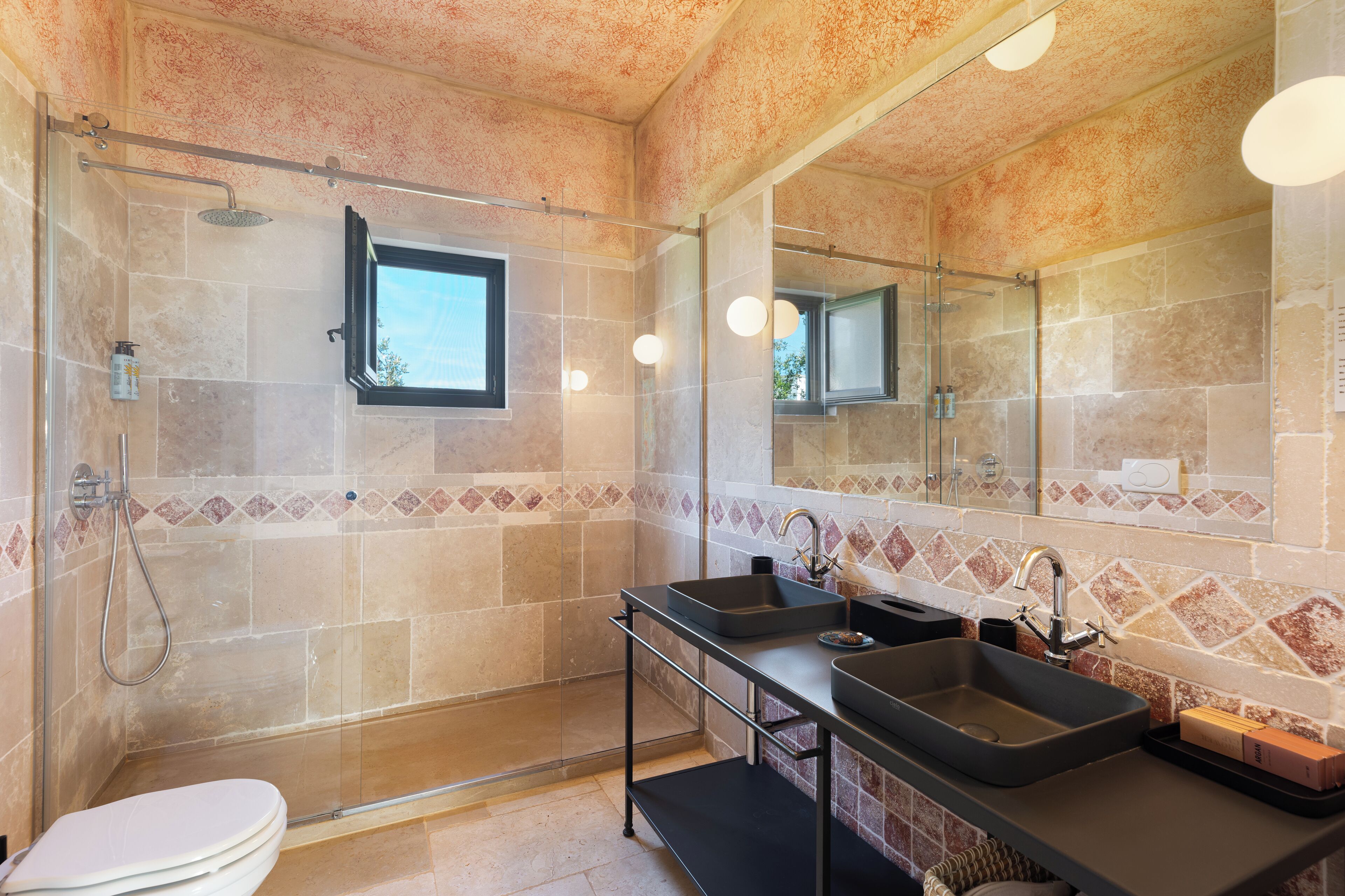 Un baño moderno con ducha envuelta en vidrio, tocador doble y un espejo grande.