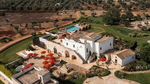 Eine Vogelperspektive zeigt eine weiße Villa mit Pool, Sitzgelegenheiten im Freien und einem gepflegten Garten.
