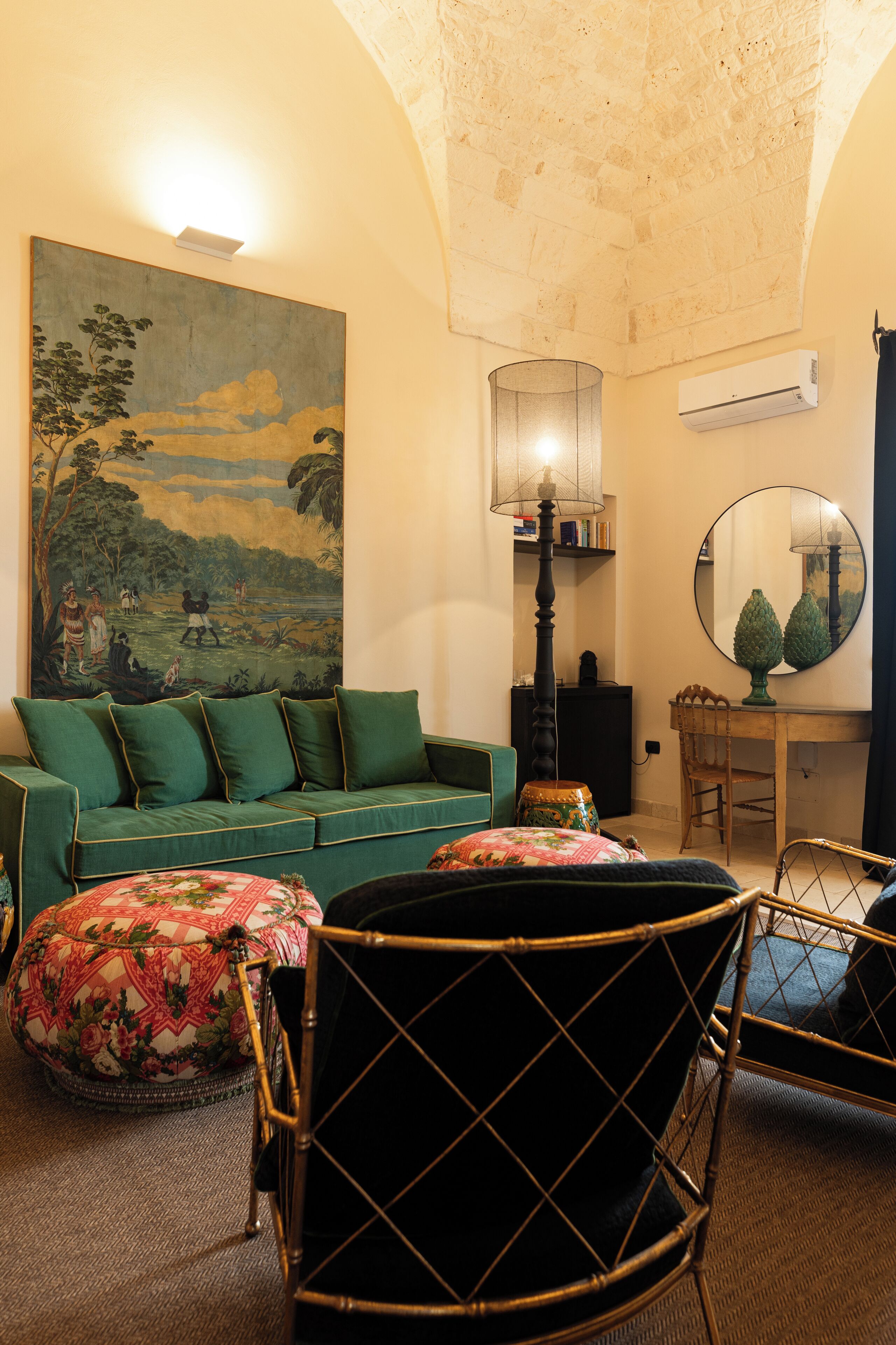 A living room with a green sofa, a black chair, a large painting, a lamp, and a mirror.